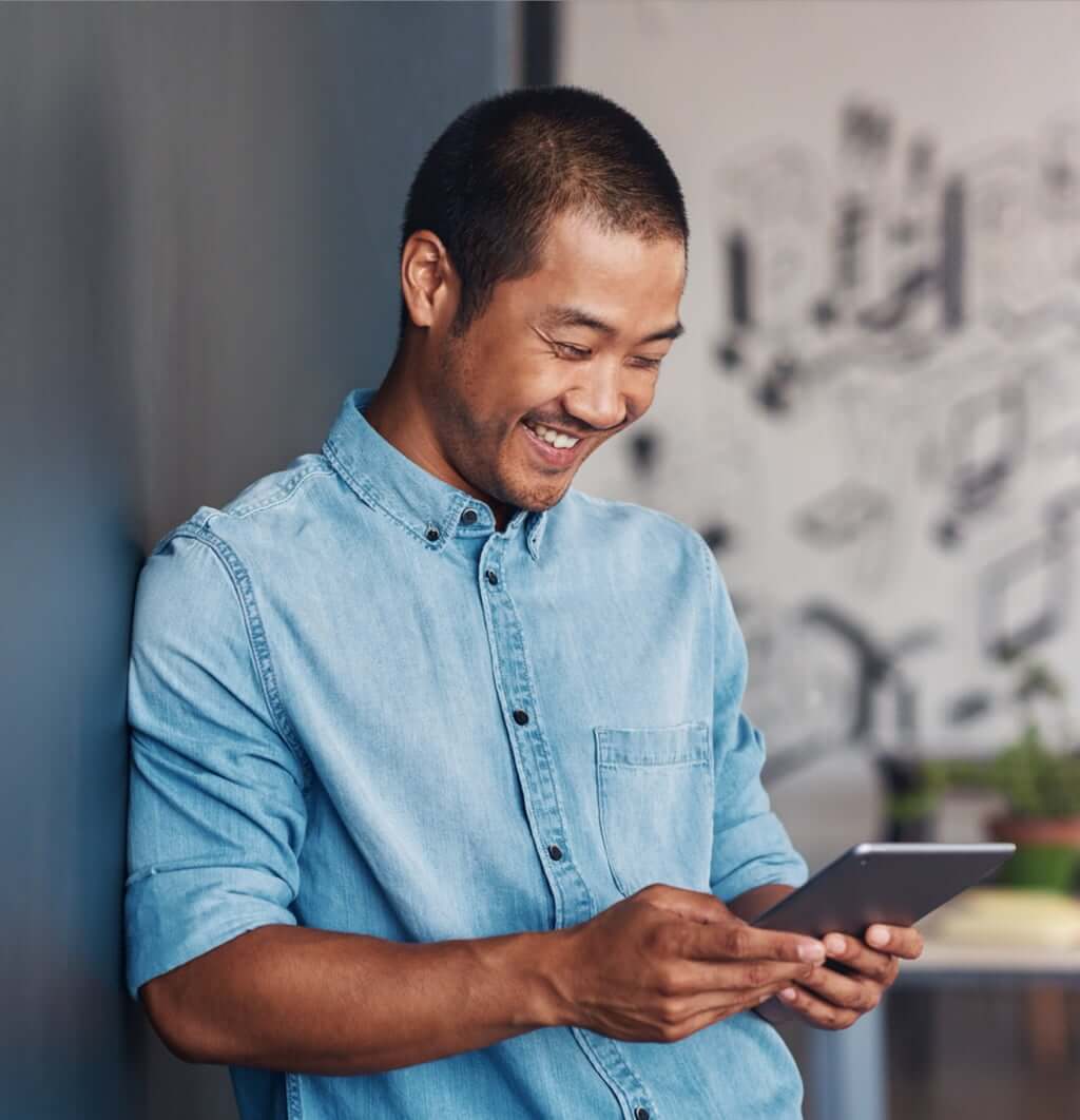 A casually dressed Digital Designer leaning against a wall using a digital tablet