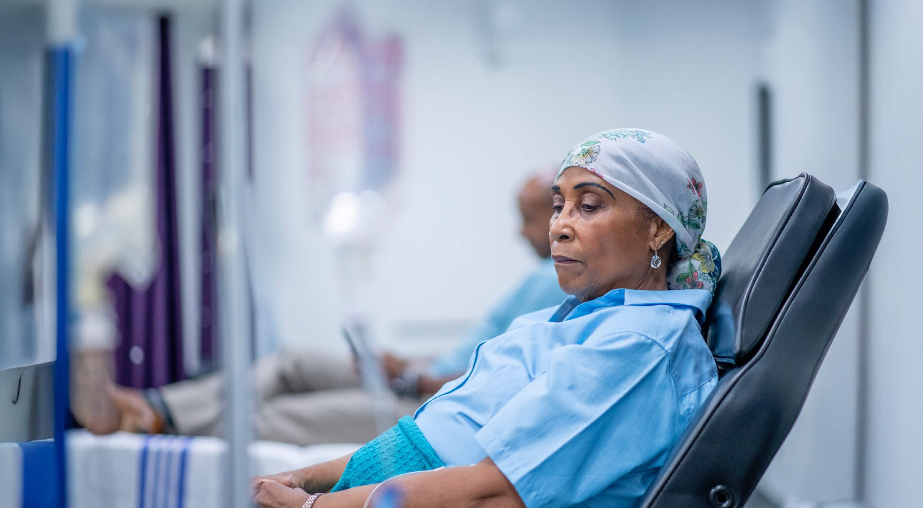 A middle-aged woman reclining in a hospital bed whilst she receives treatment