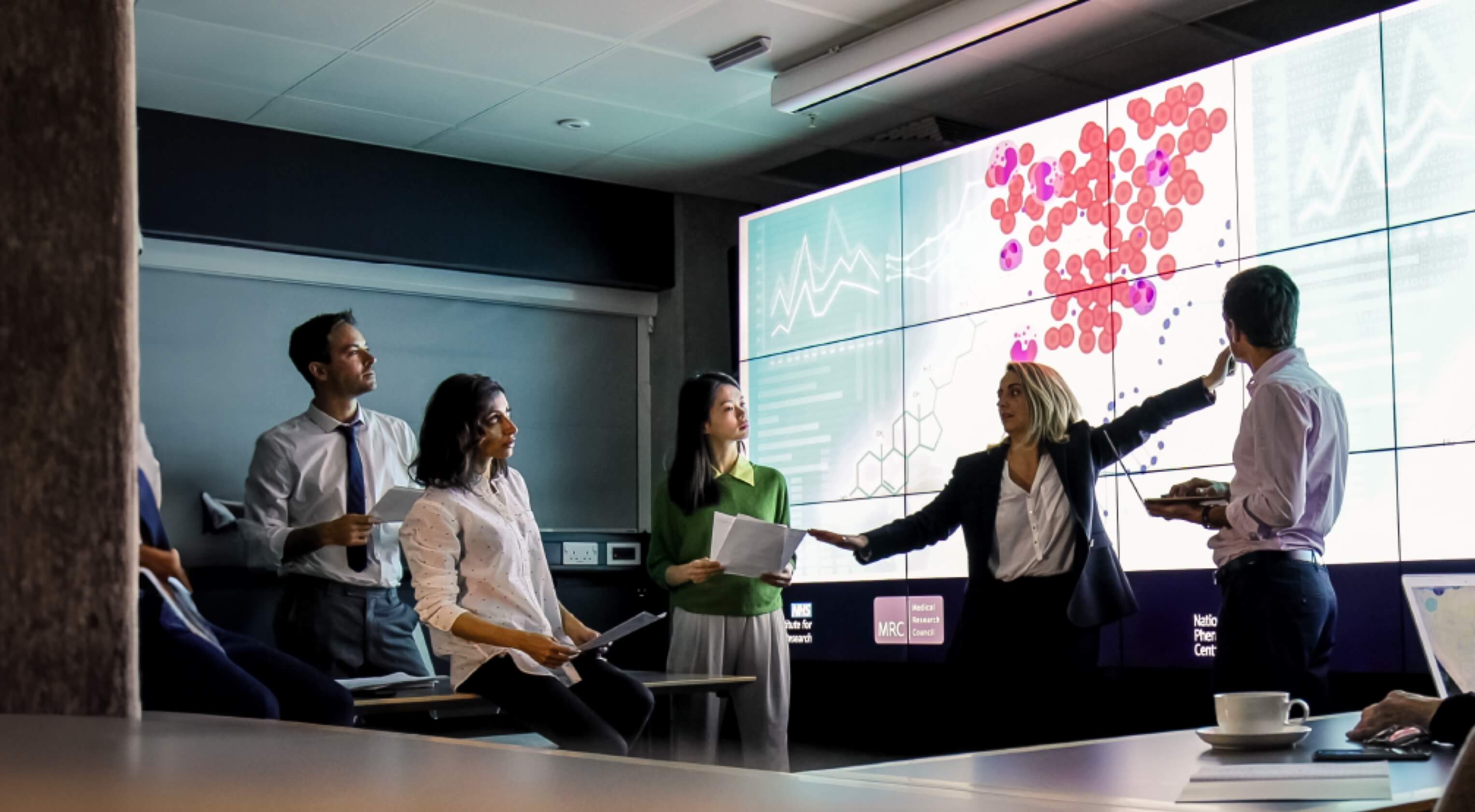 A business woman presents to her colleagues in front of a large video wall