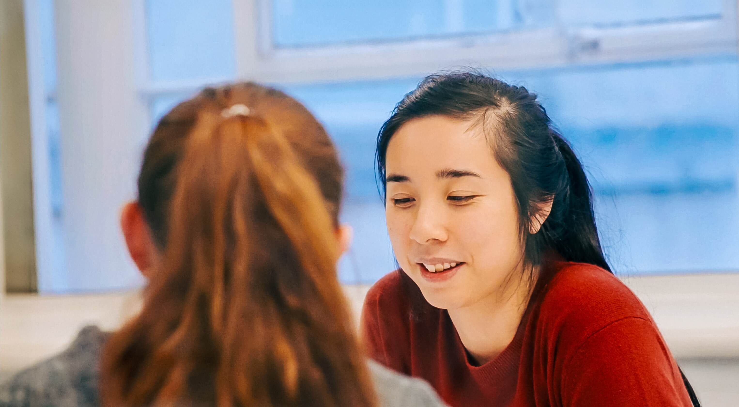 A young woman sits at a table and discusses work with another team member