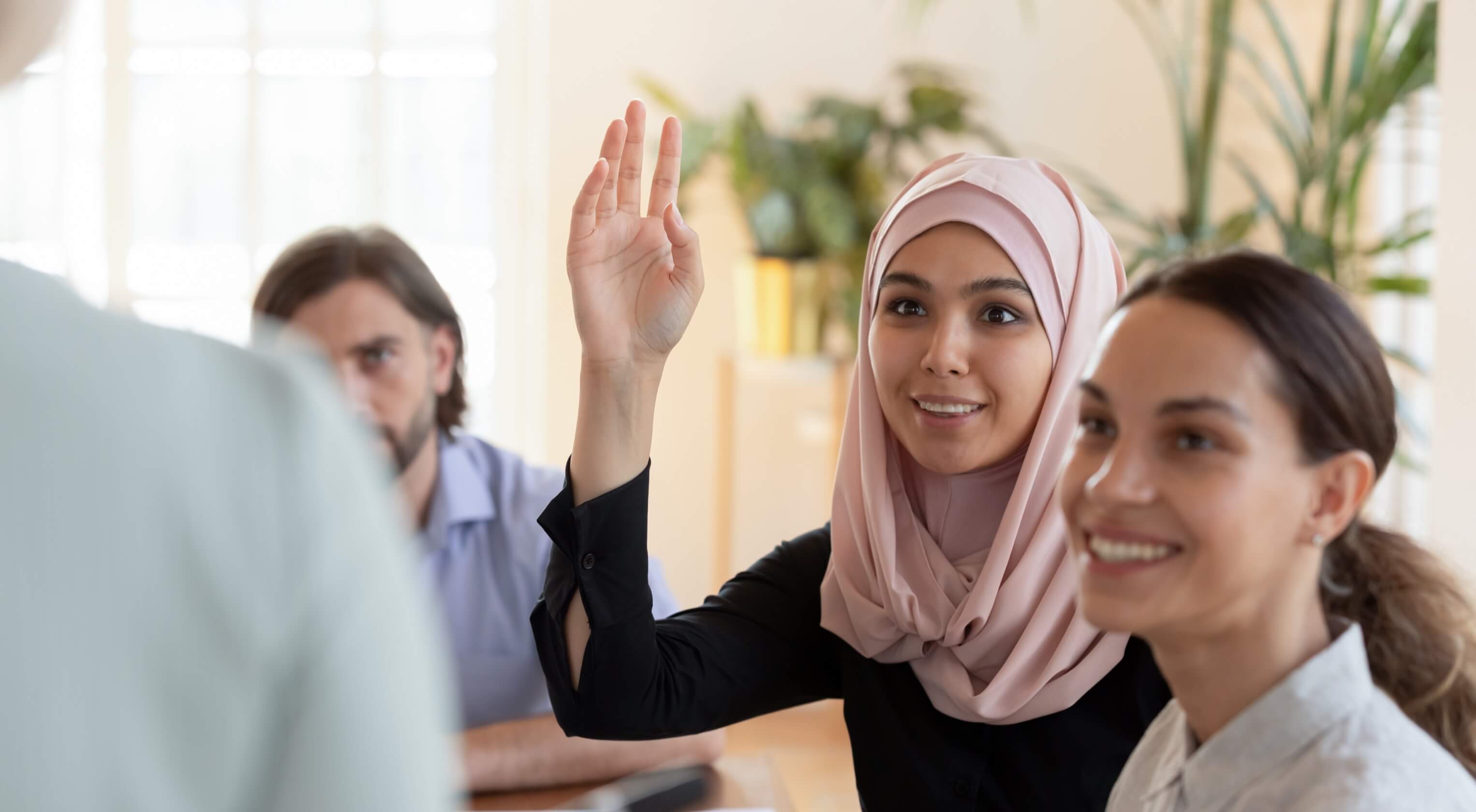  A similing young buisnesswoman raising her hand to answer a question in a team meeting