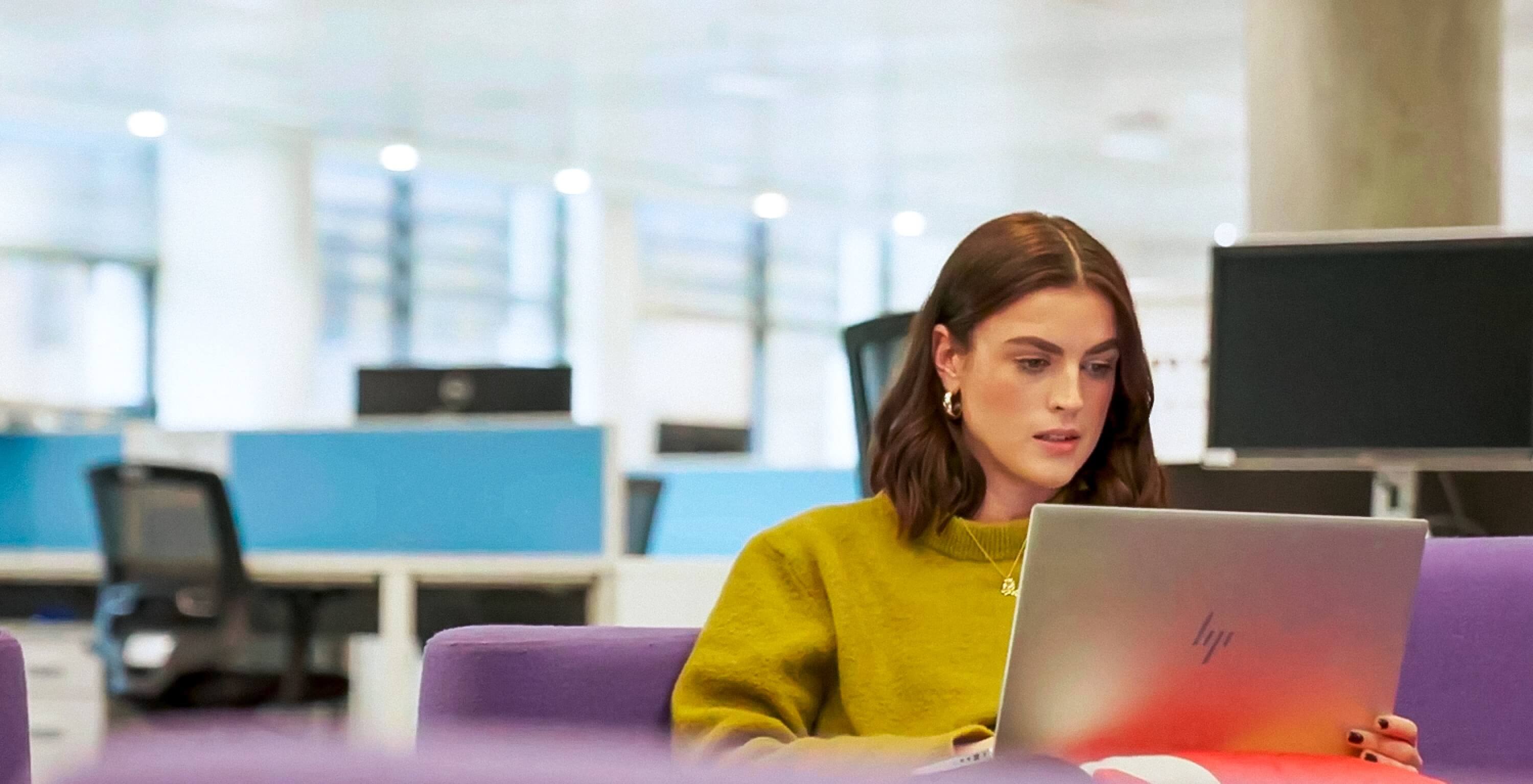 A young female intern working at a laptop computer in a breakout area