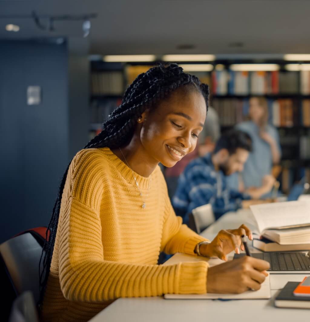 A smiling female graduate making notes whilst using a laptop computer